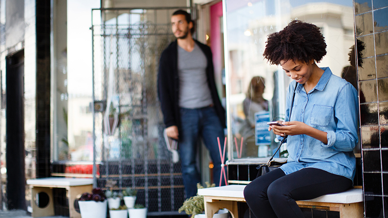 Woman sitting on a bench outside of a business while on her mobile phone.