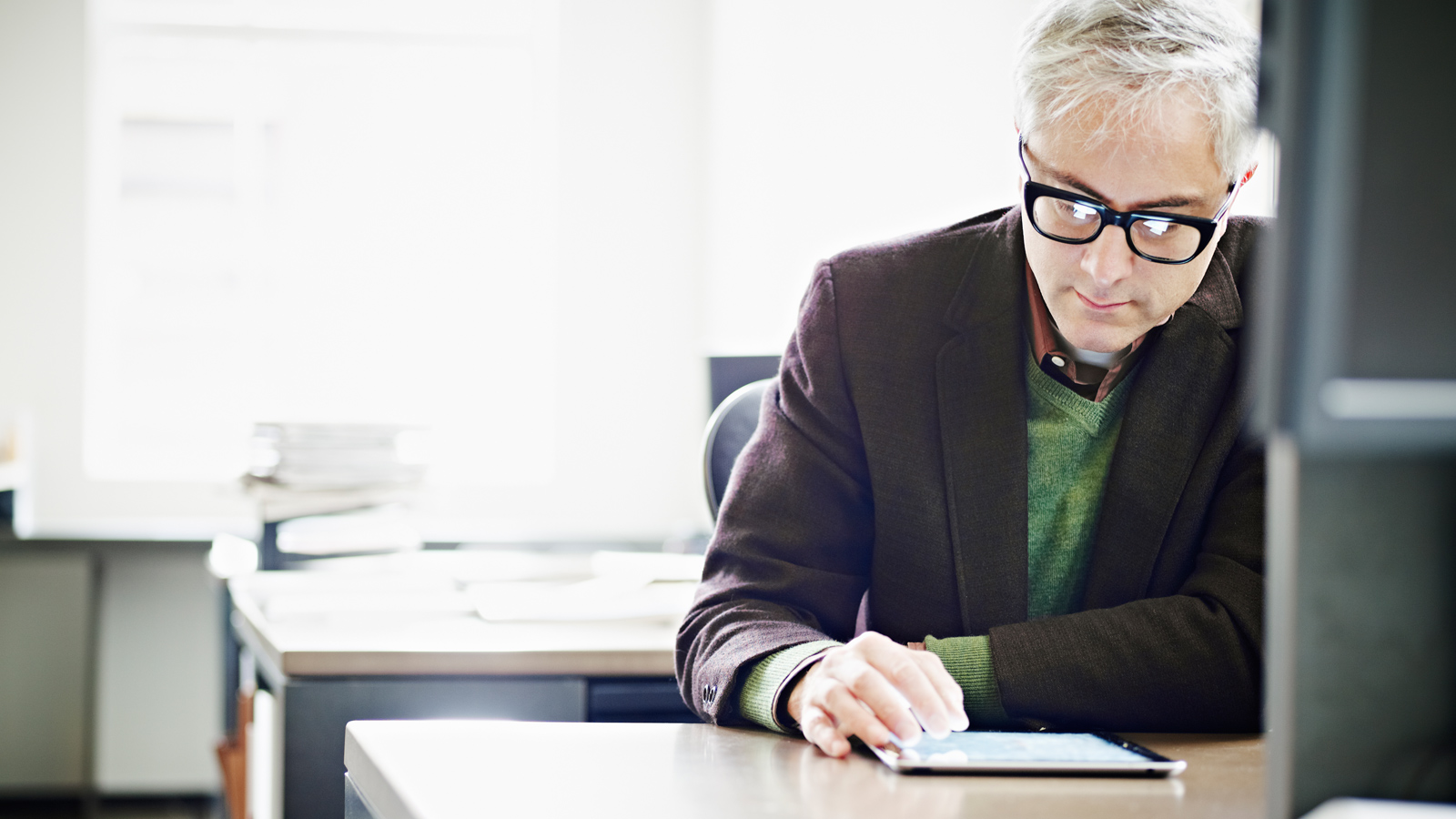 Man sitting at his desk scrolling through a tablet. 