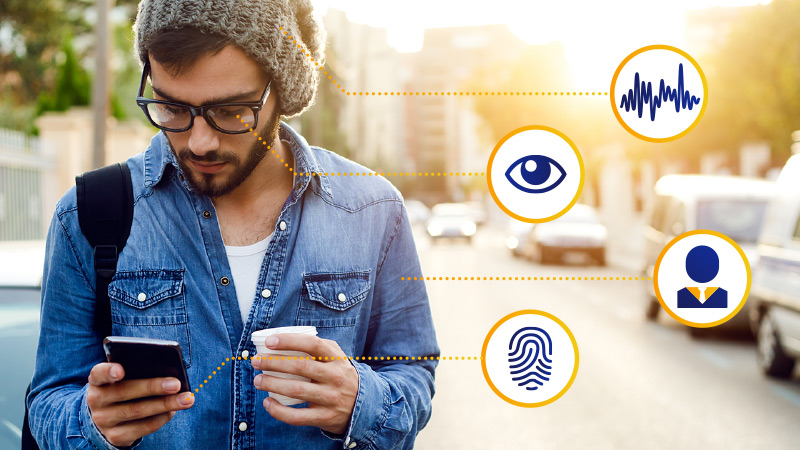 Man on city street using a smart phone with biometric symbols for voice analysis, iris recognition, behavior patterns, and fingerprint recognition.