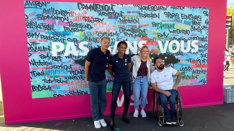 four people posing in front of paris paralympics sign
